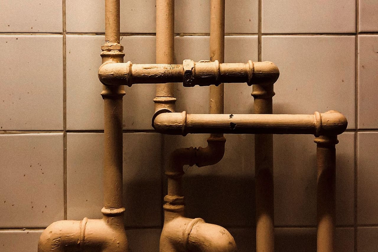 At what temperature do pipes freeze: Photograph of pipes near white tiles