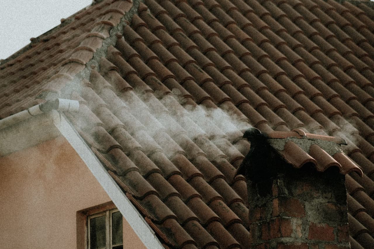 Chimney flashing leak: Smoke coming out of a brick chimney on a tiled roof