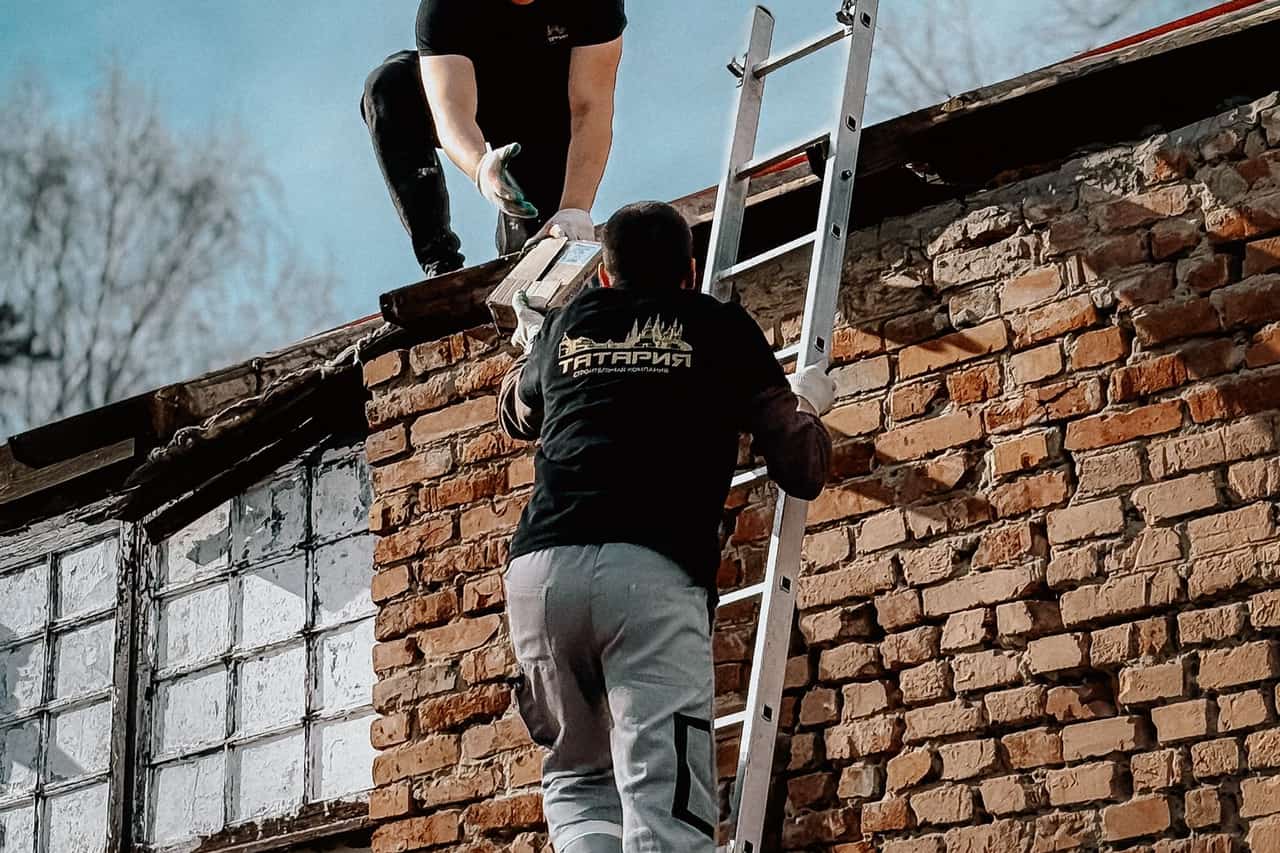 Does homeowners insurance cover a leaking roof: Construction workers climbing ladder to brick roof