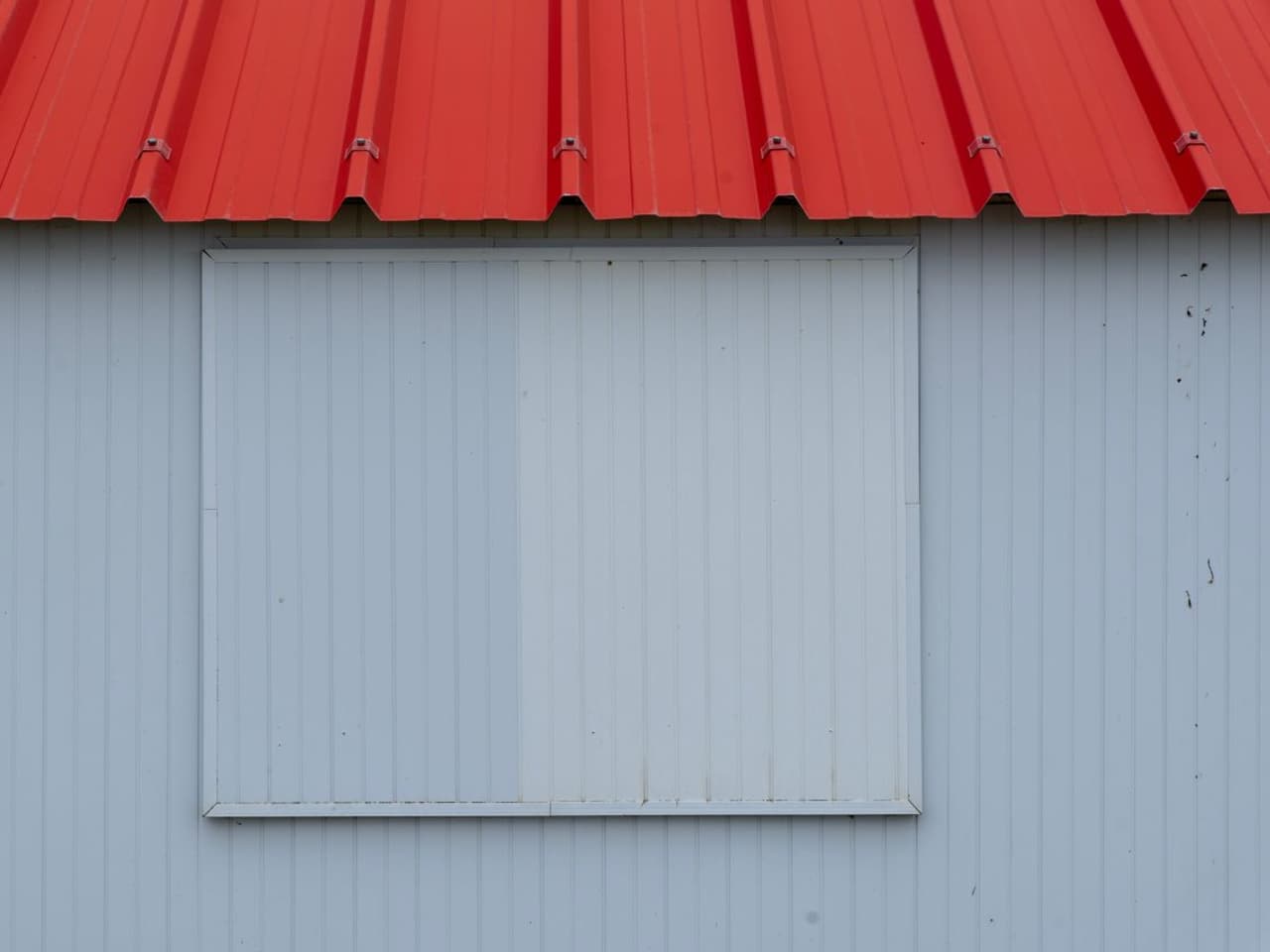 Fixing a leaking metal roof: red metal roof edge above a white metal wall panel