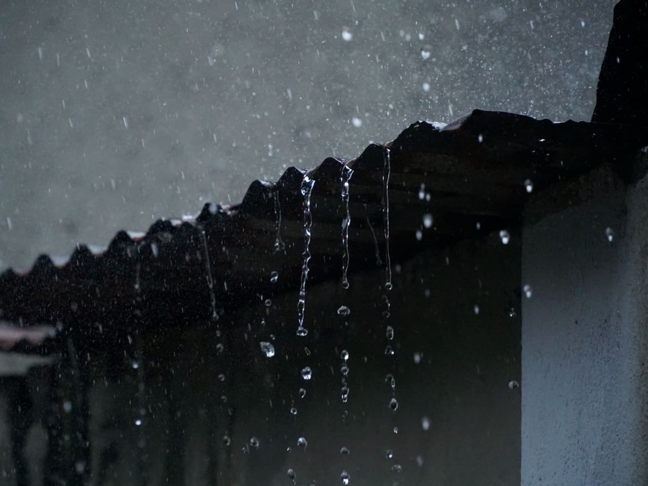 Gutter installation cost: rainwater dripping from the dark edge of a roof