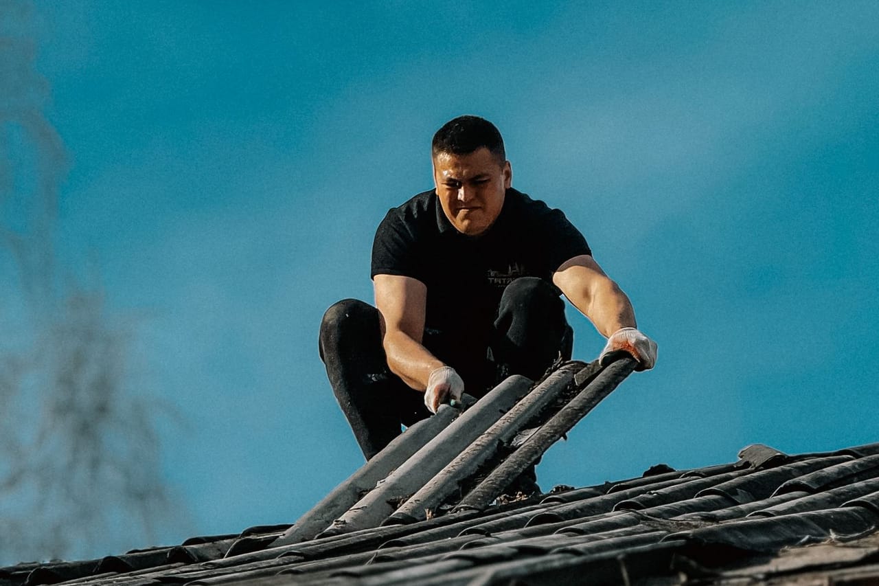 How much does replacing a roof cost: Man climbing roof ladder under clear sky