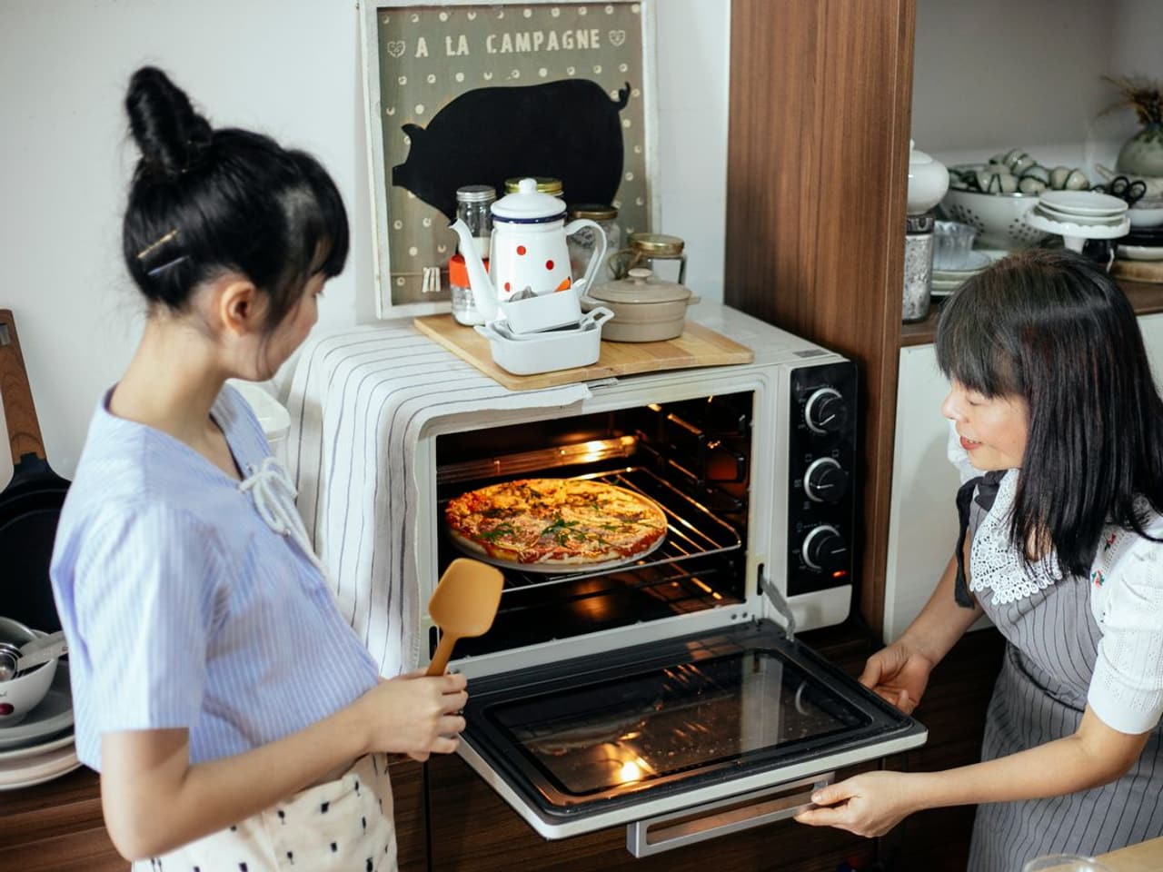 How to clean an electric stove top: woman pulling a tray from a countertop electric oven