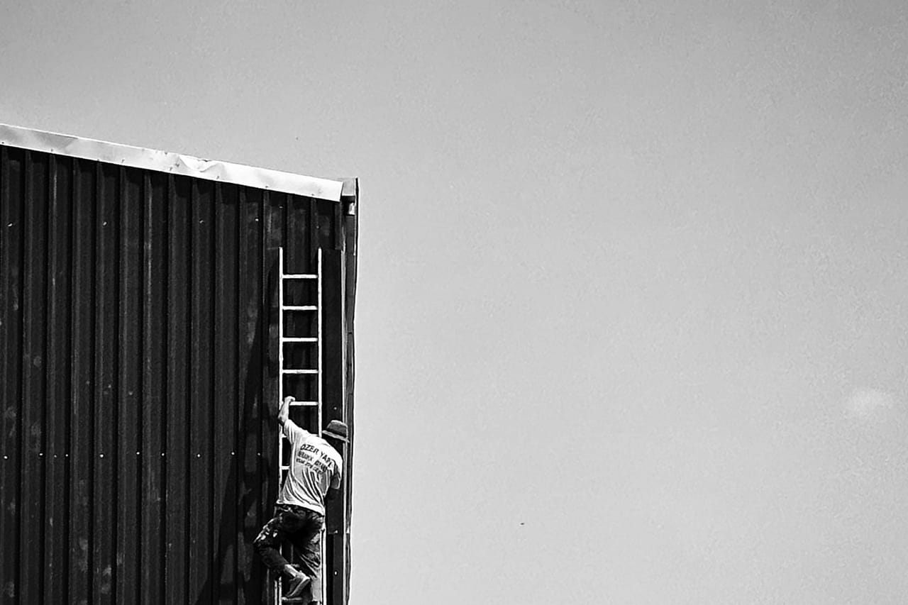 How to clean gutters: Black and white roofer climbing ladder