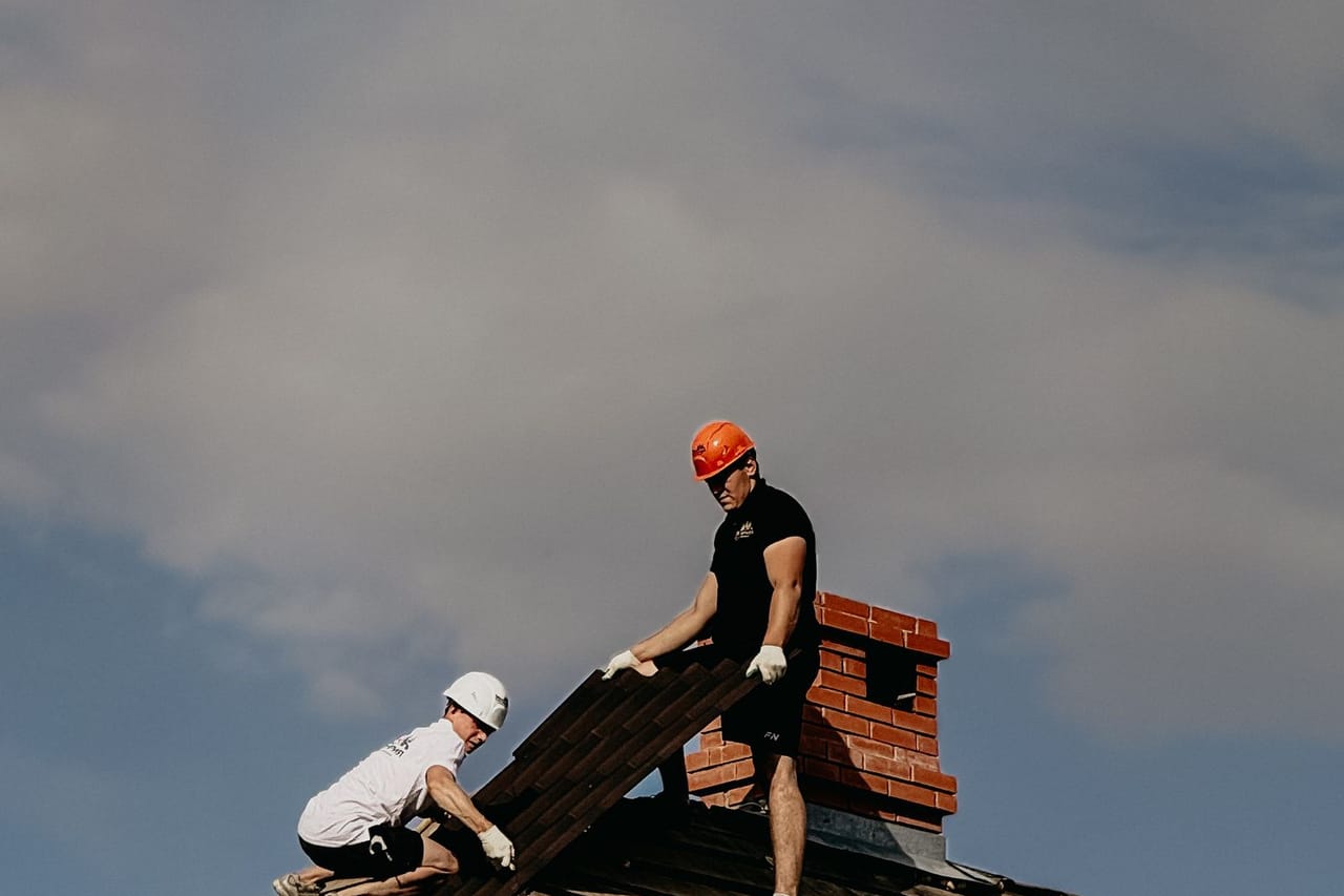 How to find where your roof is leaking: Construction workers repairing roof under cloudy sky