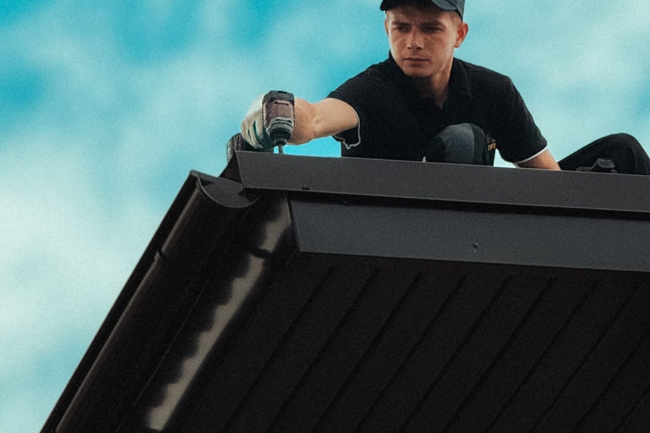 Roof inspection after storm: Roofer working on house roof against clear sky