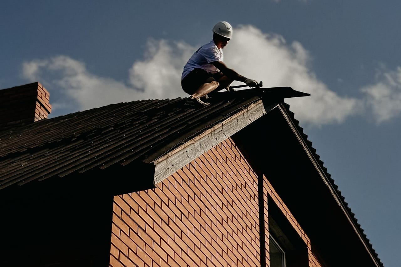 Roof leak repair prices: Worker repairing roof on brick house