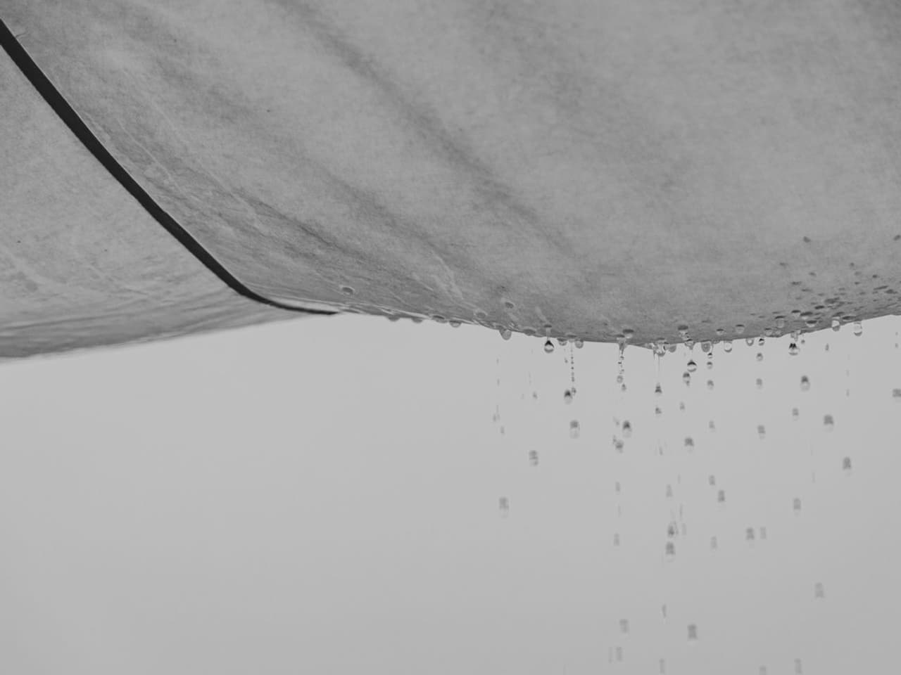 Roof leaking in heavy rain: water drops falling from a grey ceiling