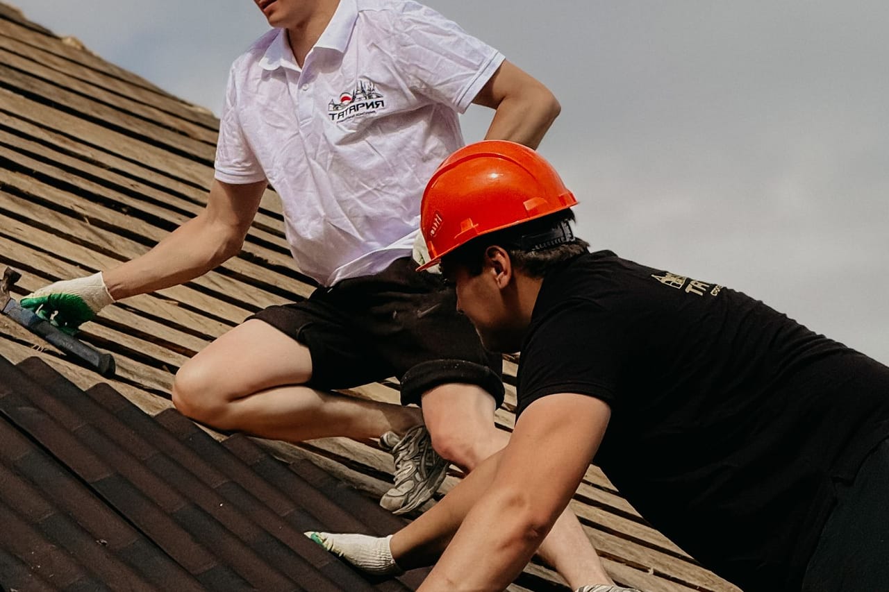 Roof overlay vs tear off: Construction workers repairing roof with safety gear