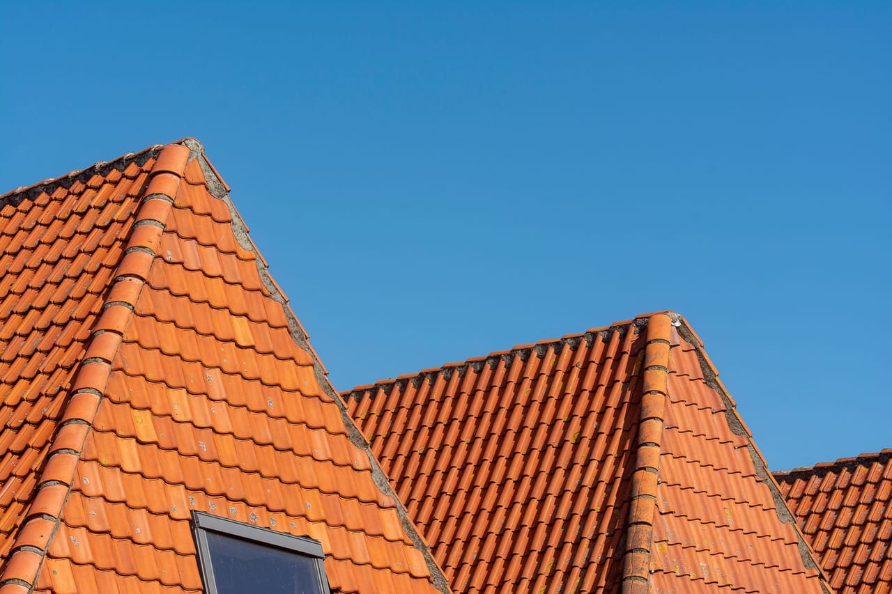 Roof replacement cost per square foot: Red roof tiles against clear blue sky