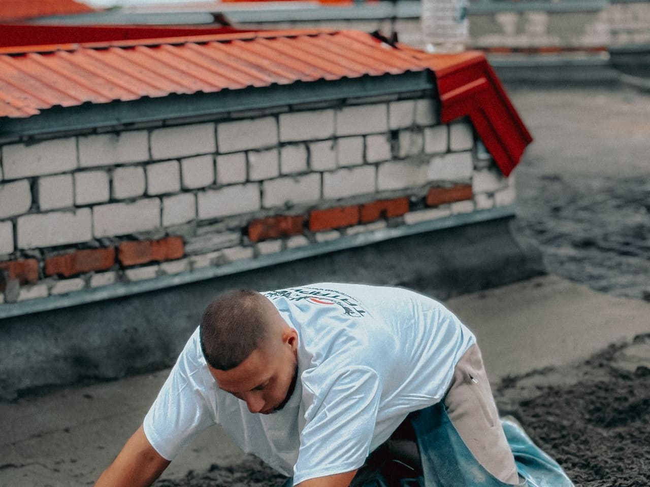 Sewer line replacement cost: worker kneeling beside a brick wall on a construction site