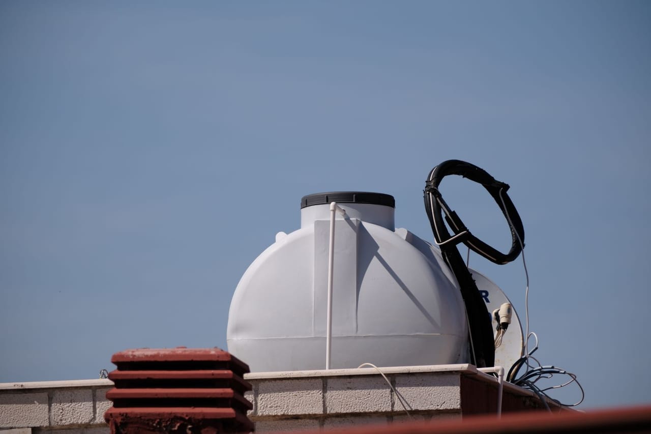 Tankless vs tank water heater: Rooftop water tank against blue sky