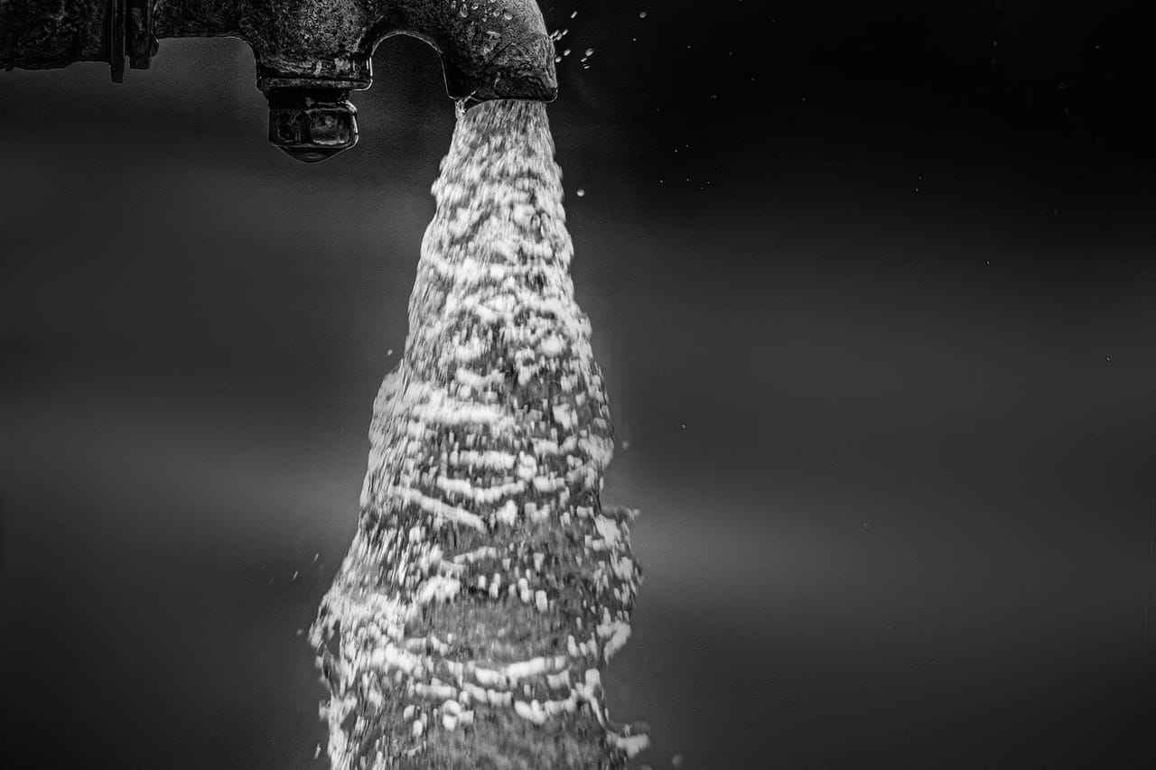 Water heater popping noise: Black and white shot of water flowing from a tap