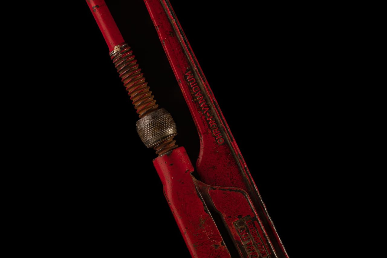 What to do when a pipe bursts in your house: Vintage red pipe wrench on black background