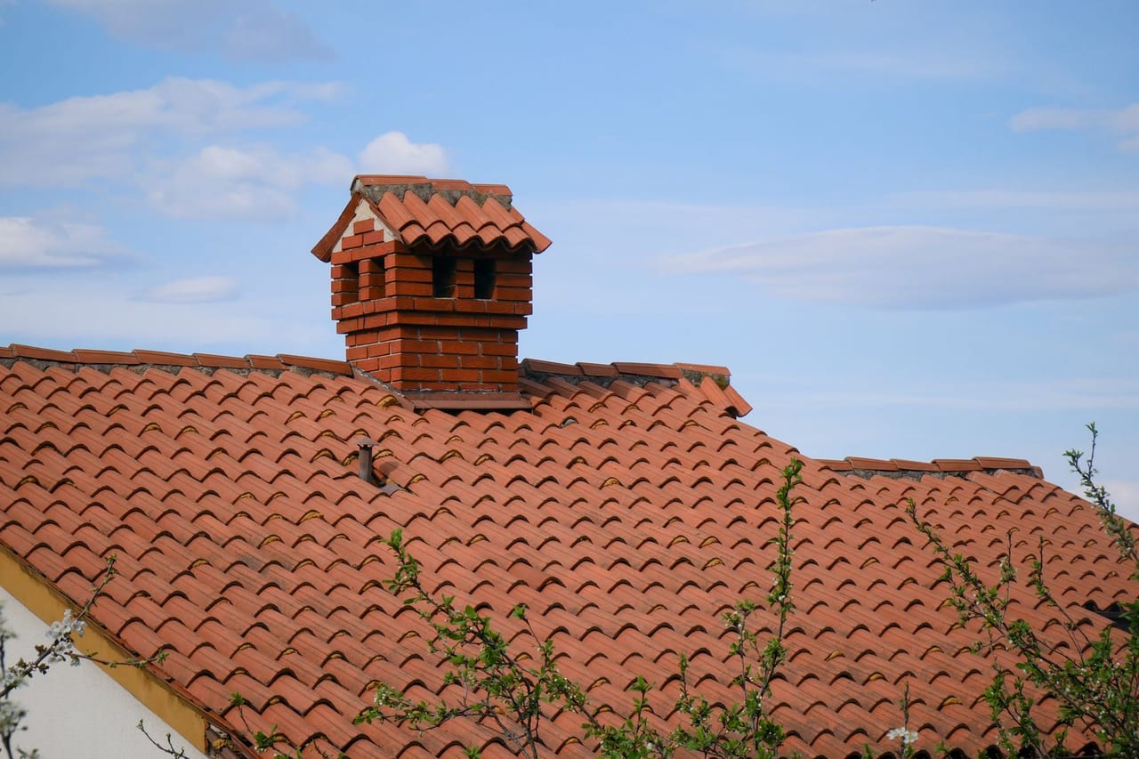 When to replace a roof: Red brick chimney on tiled roof against blue sky