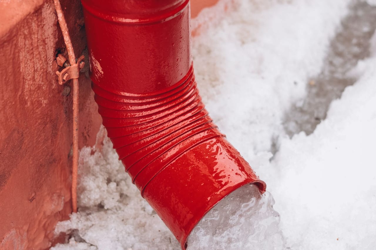 Plumber Casper WY: Red drainpipe with melting snow during winter