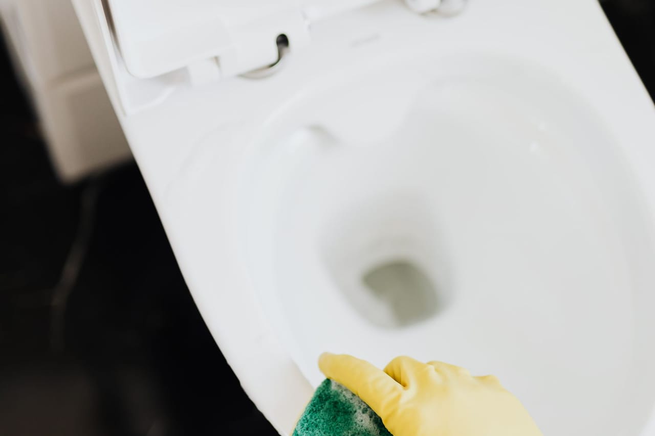 Plumber Concord NH: Crop person cleaning toilet rim with sponge