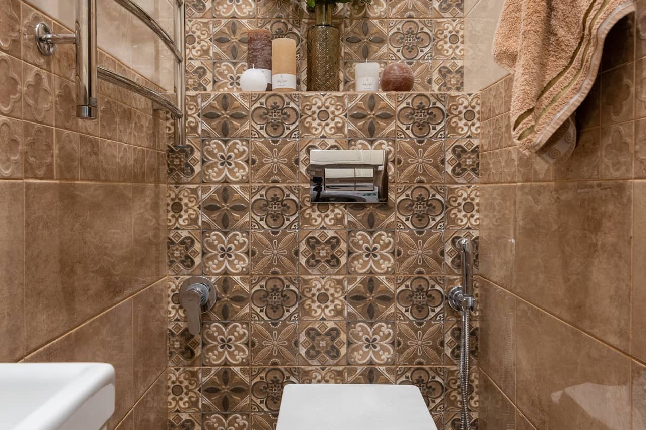 Plumber Melbourne FL: White ceramic toilet bowl in brown tiled wall water closet