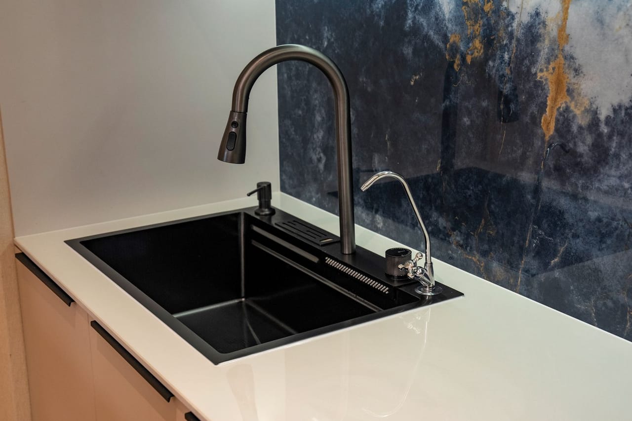 Plumber Sumter SC: Modern kitchen faucet with black sink and marble backsplash