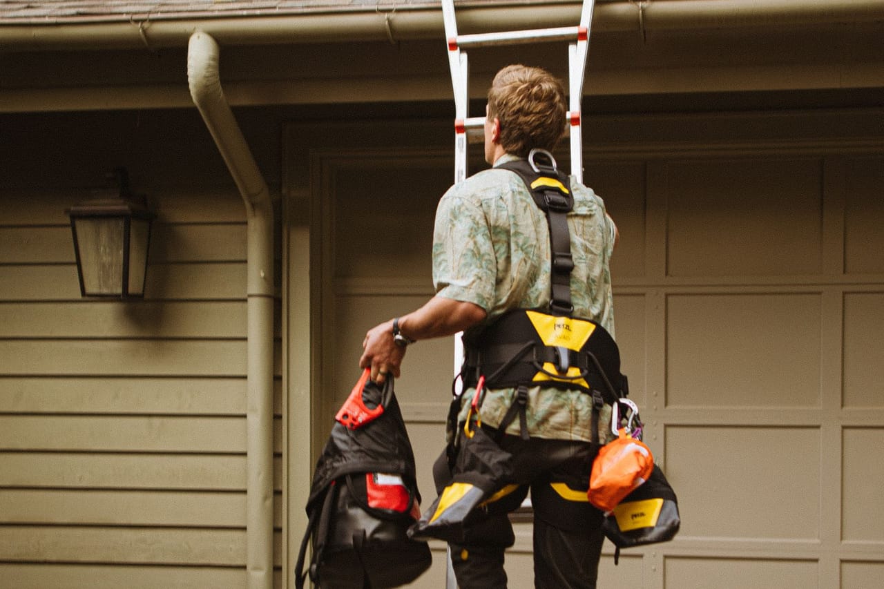Roof repair Austin TX: Roofer with safety gear ascending ladder for repair