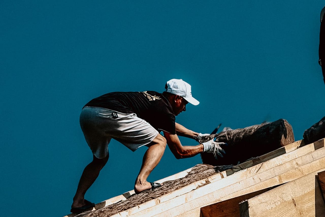 Roof repair Bloomington IN: Roof construction worker in action against clear sky