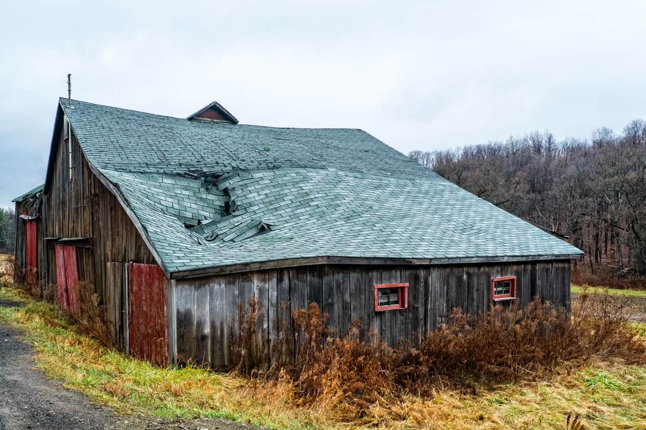 Roof repair Broken Arrow OK: Damaged roof tiles of a brown wooden barn house