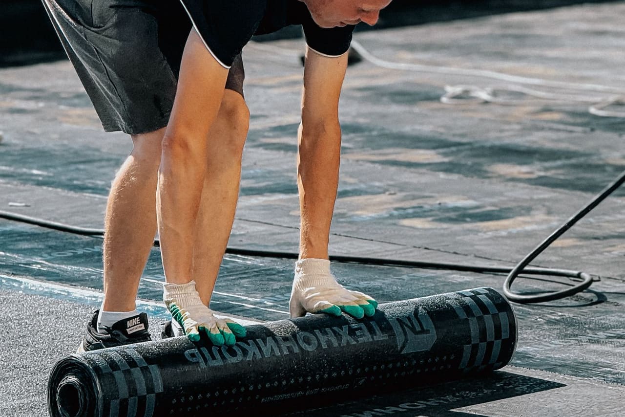 Roof repair Palm Springs CA: Man installing roofing felt on building rooftop