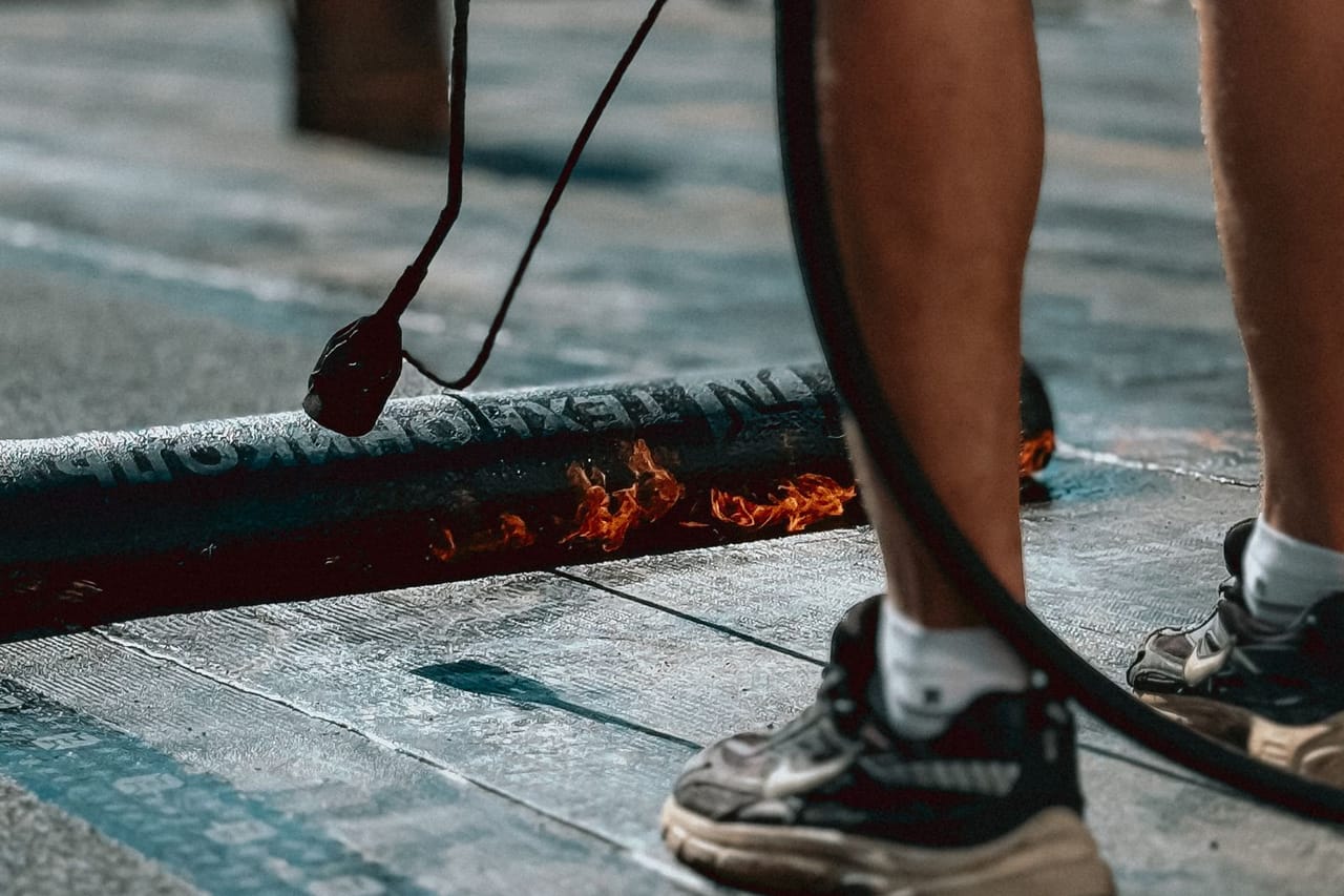 Roof repair Pueblo CO: Worker applying asphalt on rooftop with flame torch