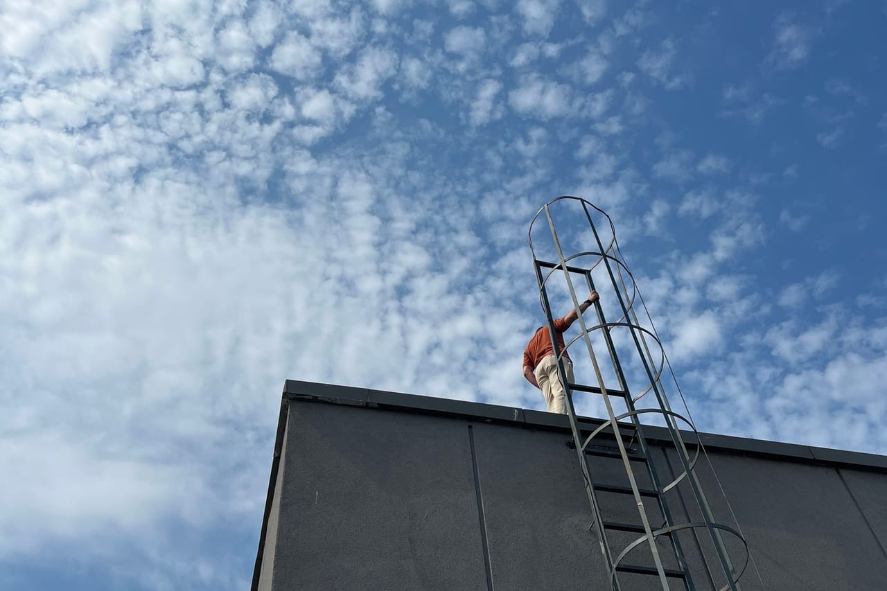 Roof repair Sarasota FL: Person climbing rooftop ladder against cloudy sky