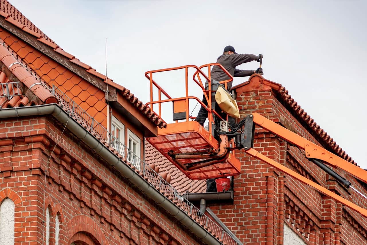 Roof repair St Petersburg FL: Roofer performing maintenance on red brick building