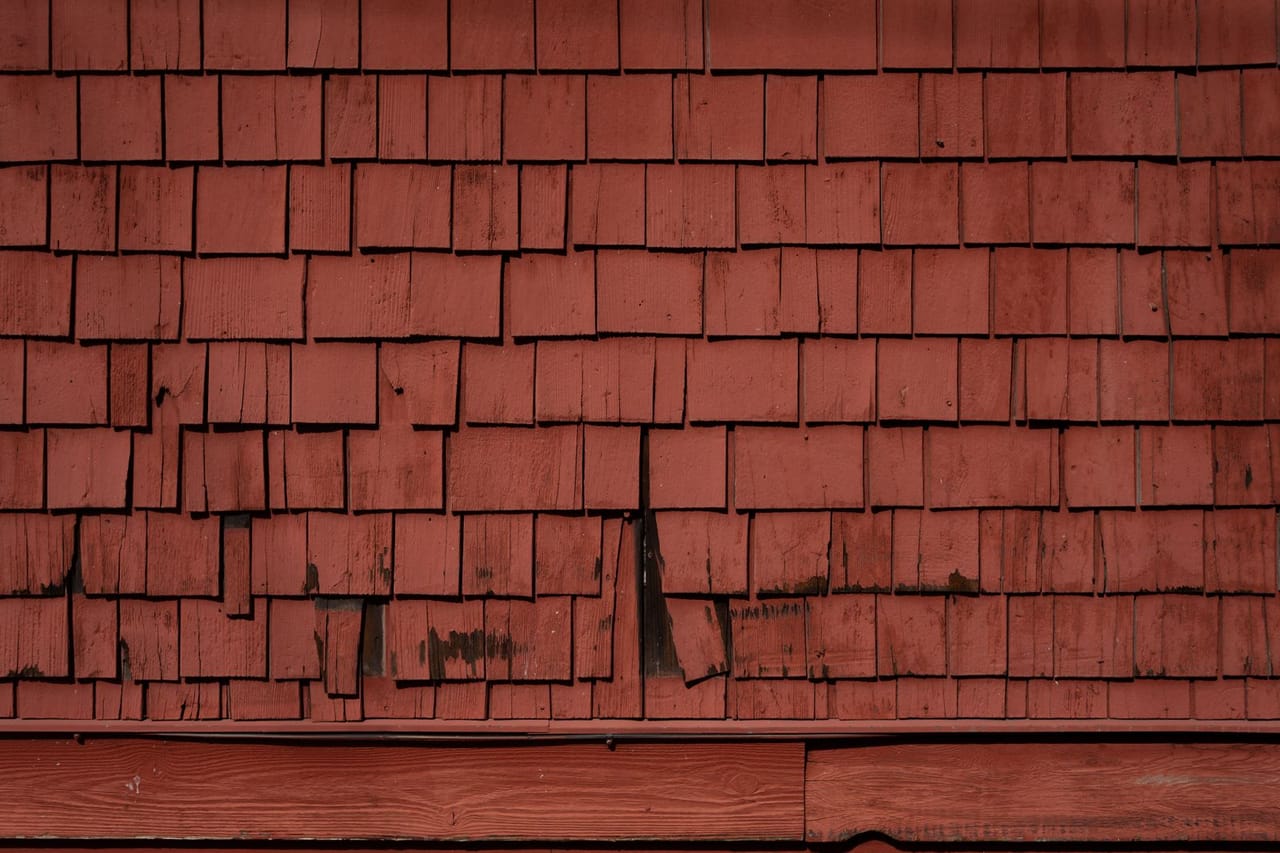Roof repair Tyler TX: Weathered red wooden shingles on building exterior